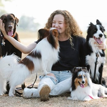 A woman sits on the ground surrounded by her dogs, enjoying a moment of relaxation outdoors.
